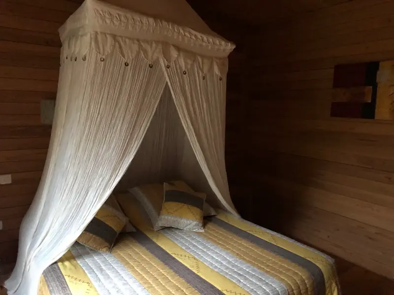 Chambre d'hôtes à Grand Bassin : lit 160 × 200 sous ciel de lit dans le bungalow en bois Les Mimosas
